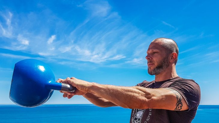 man wearing black shirt holding kettle bell near body of water