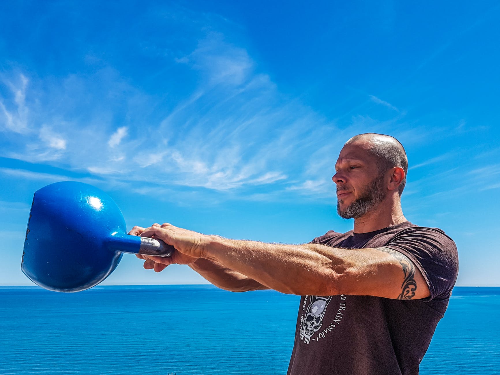 man wearing black shirt holding kettle bell near body of water